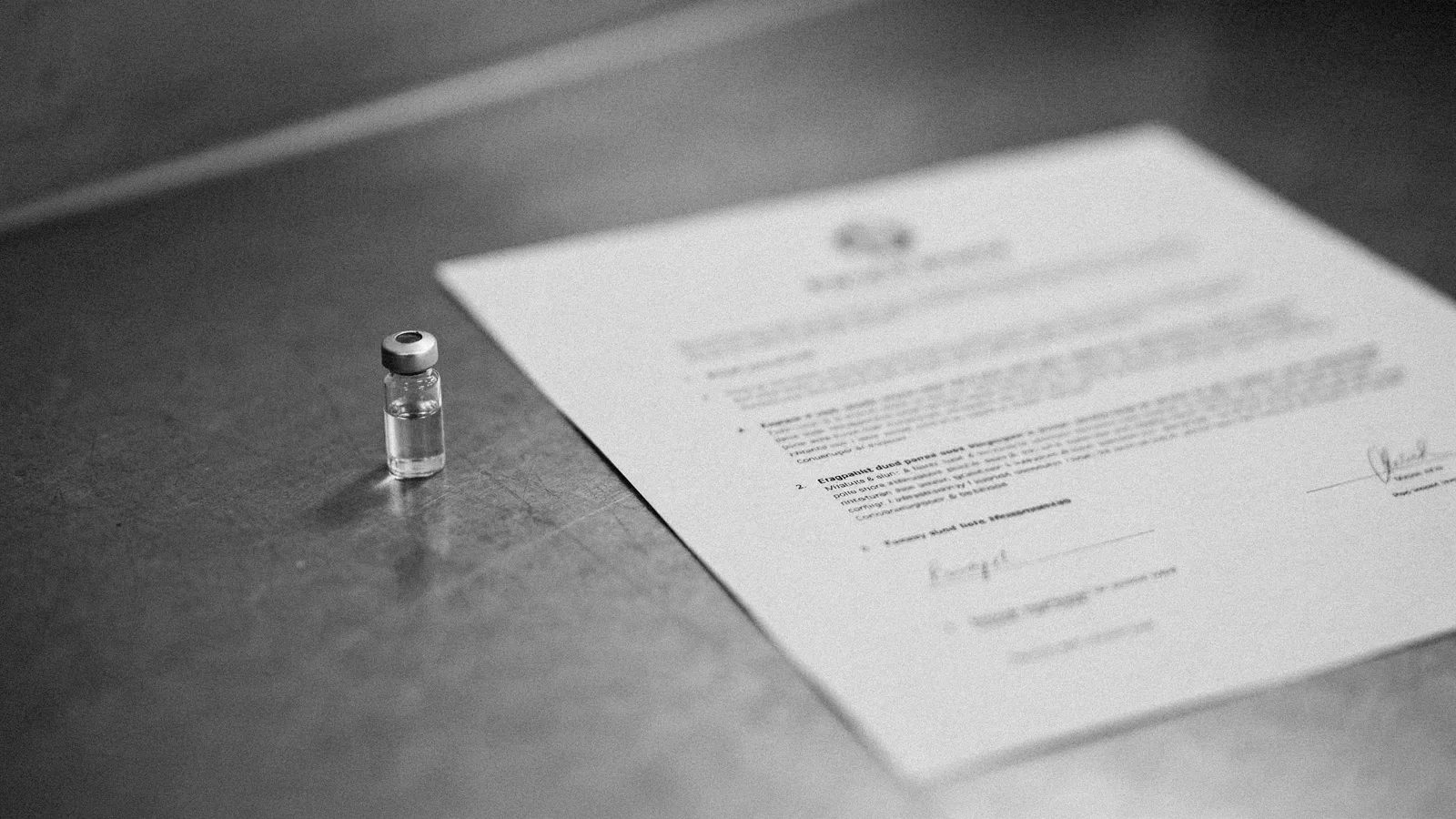 A printed certificate lying on a steel laboratory bench beside a single capped glass vial, the print out of focus